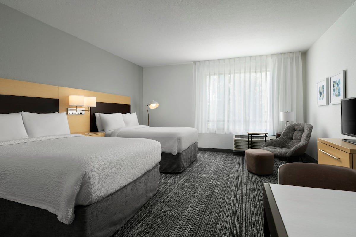 Hotelkamer met twee bedden, een bureau, een stoel, een televisie en een raam met gordijnen.