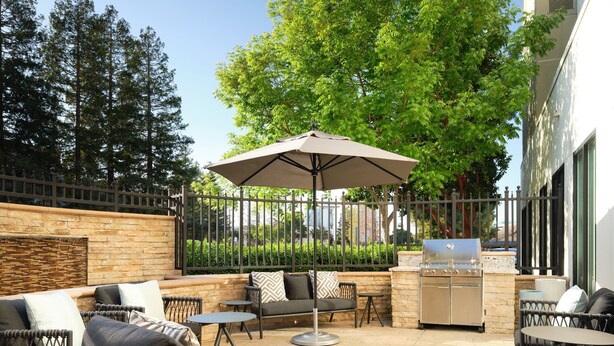 Un espace extérieur aménagé en terrasse, avec des meubles en osier, un barbecue et un grand parasol.