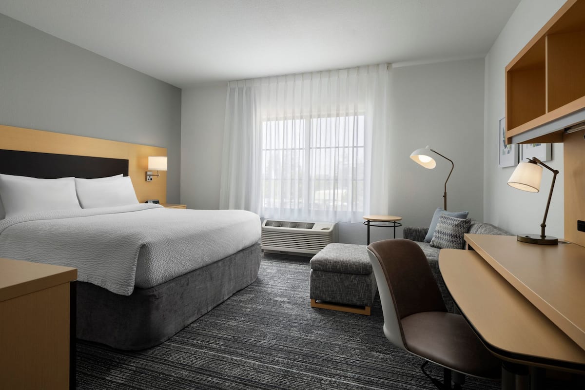 Hotelkamer met een bed, bureau, stoel, lamp en raam met gordijnen.
