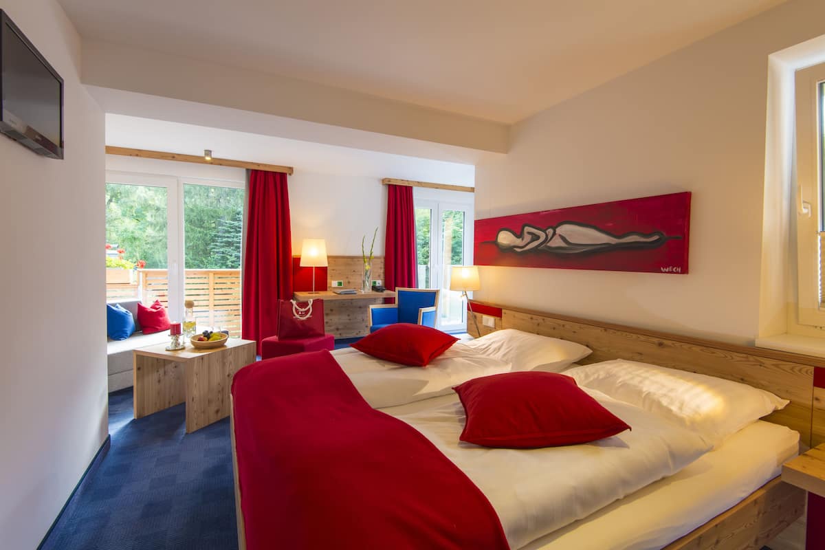 A hotel room with a bed, a desk, a chair, and a window with red curtains.