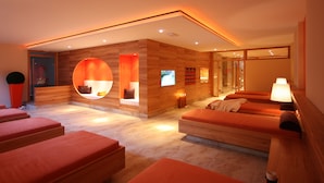 Un cuarto de spa con paredes de madera, zonas de estar circulares y una pantalla de televisión.