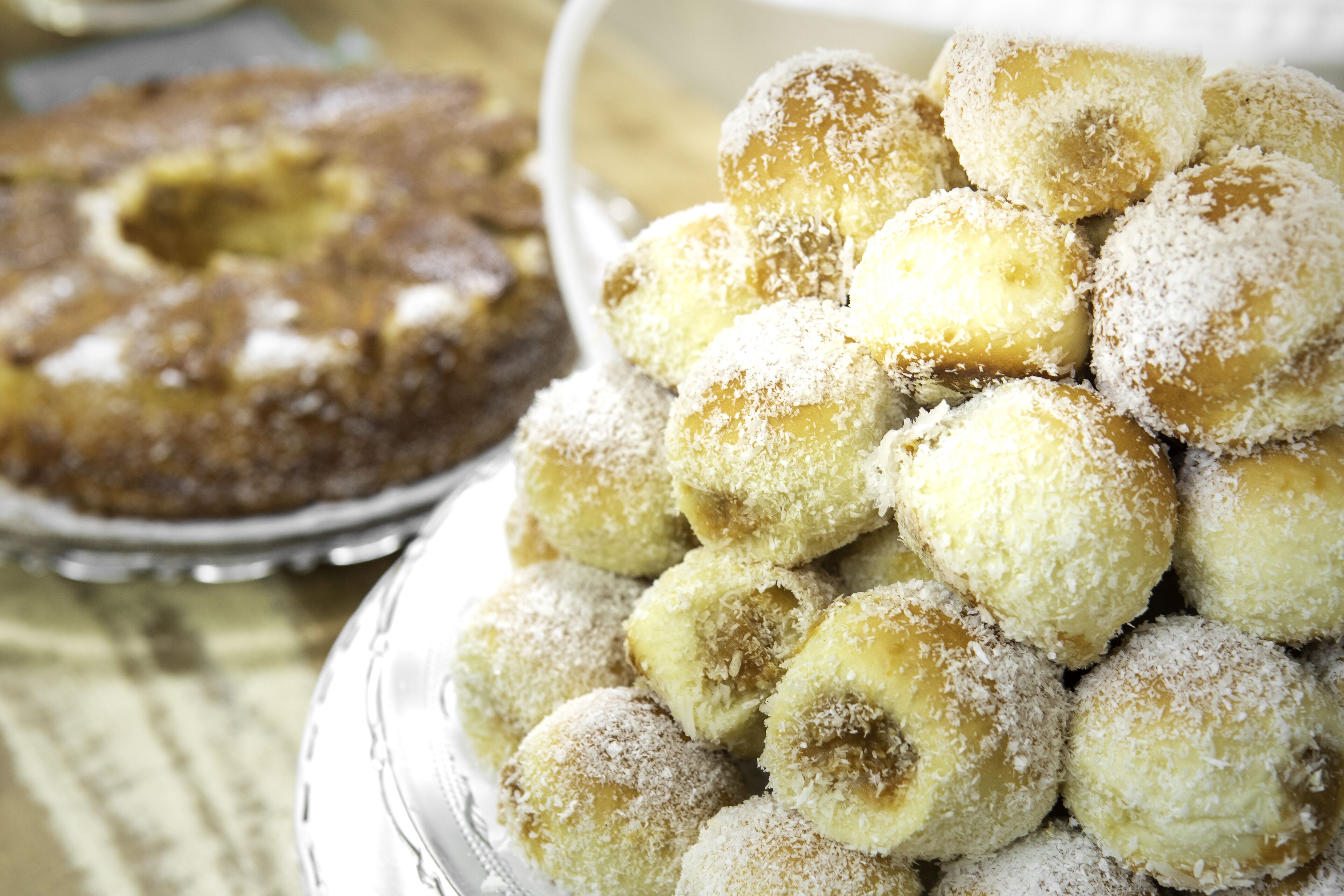 Um prato com bolinhos redondos cobertos de coco e um bolo com um buraco no centro.