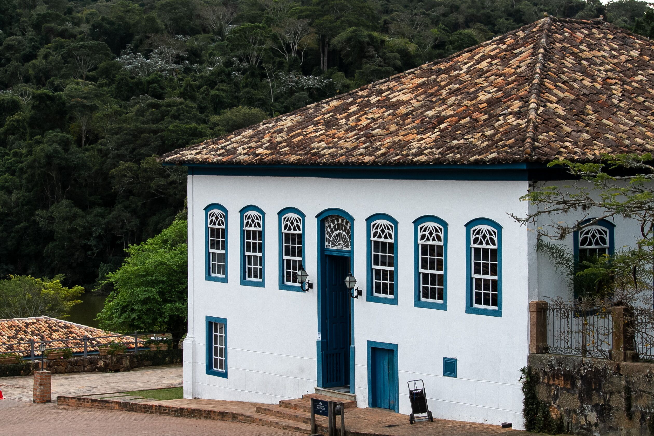 A white building with blue trim and a tiled roof, surrounded by greenery.