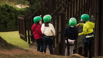 A group of people wearing helmets and harnesses, standing on a wooden bridge with a wooden fence in the background.