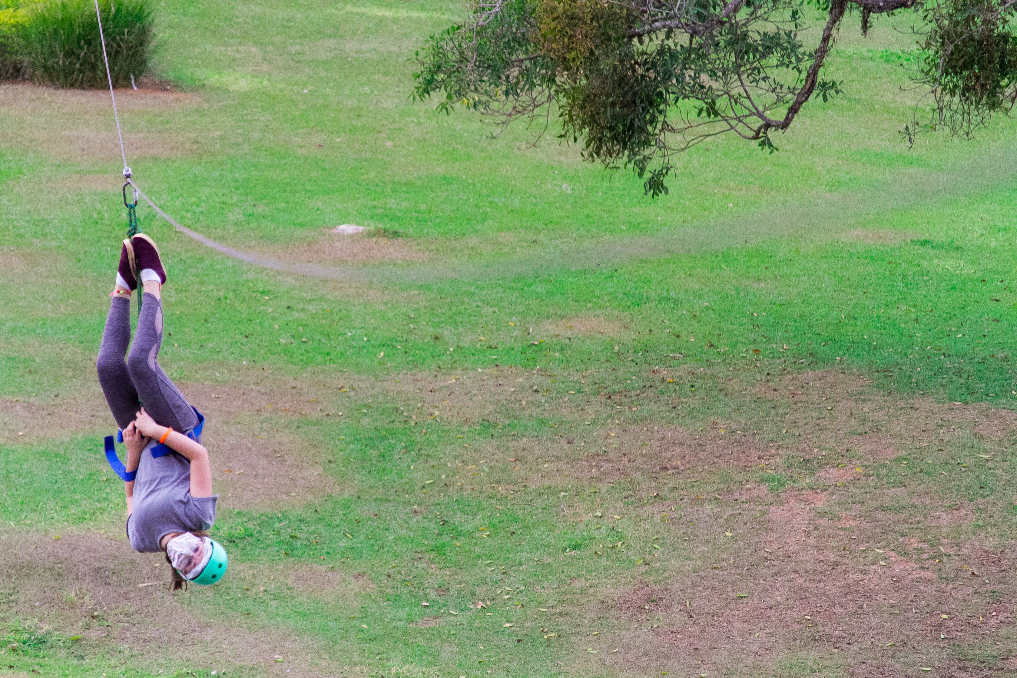 Uma pessoa está de cabeça para baixo em um balanço, em uma área gramada.