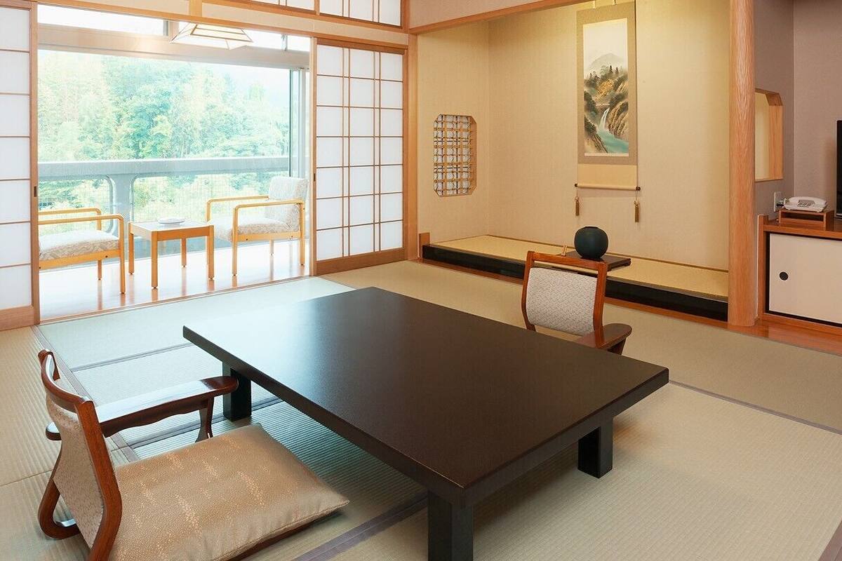 A traditional Japanese room with tatami flooring, a low table, chairs, a television, and artwork on the walls.
