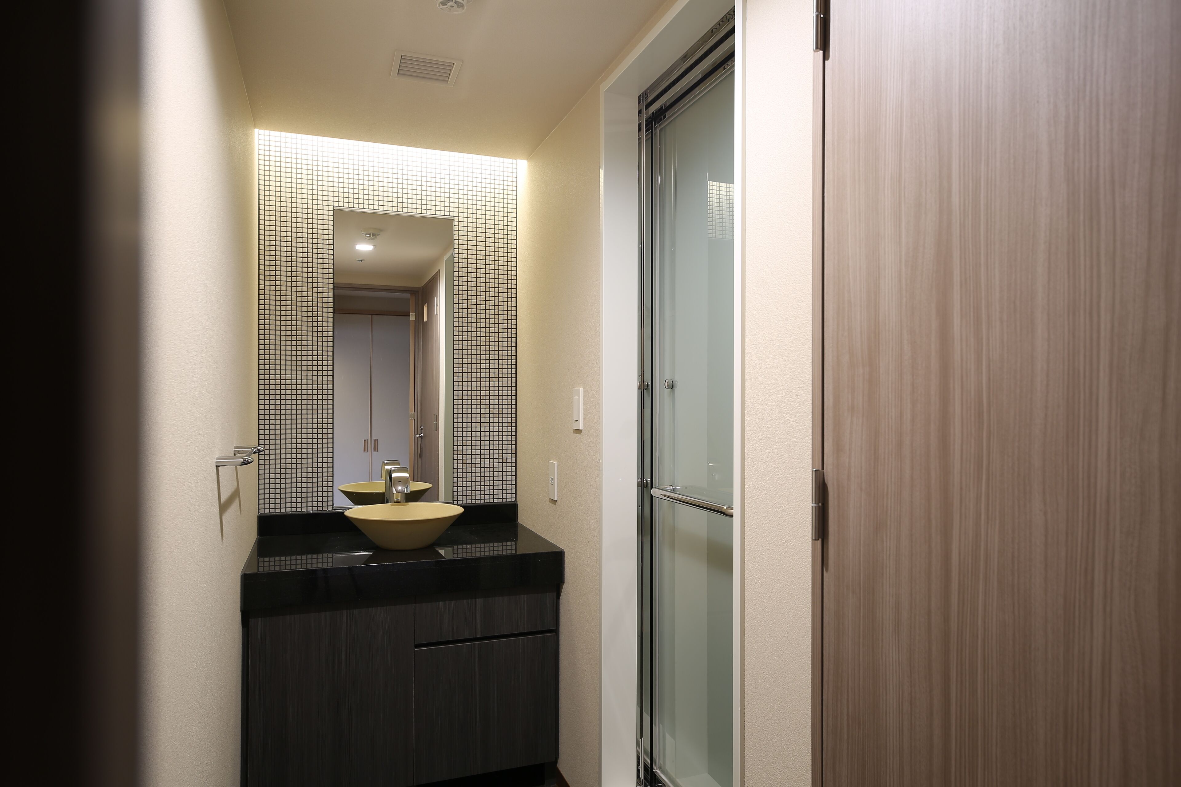 A modern bathroom with a dark countertop, a beige sink, and a glass shower enclosure.