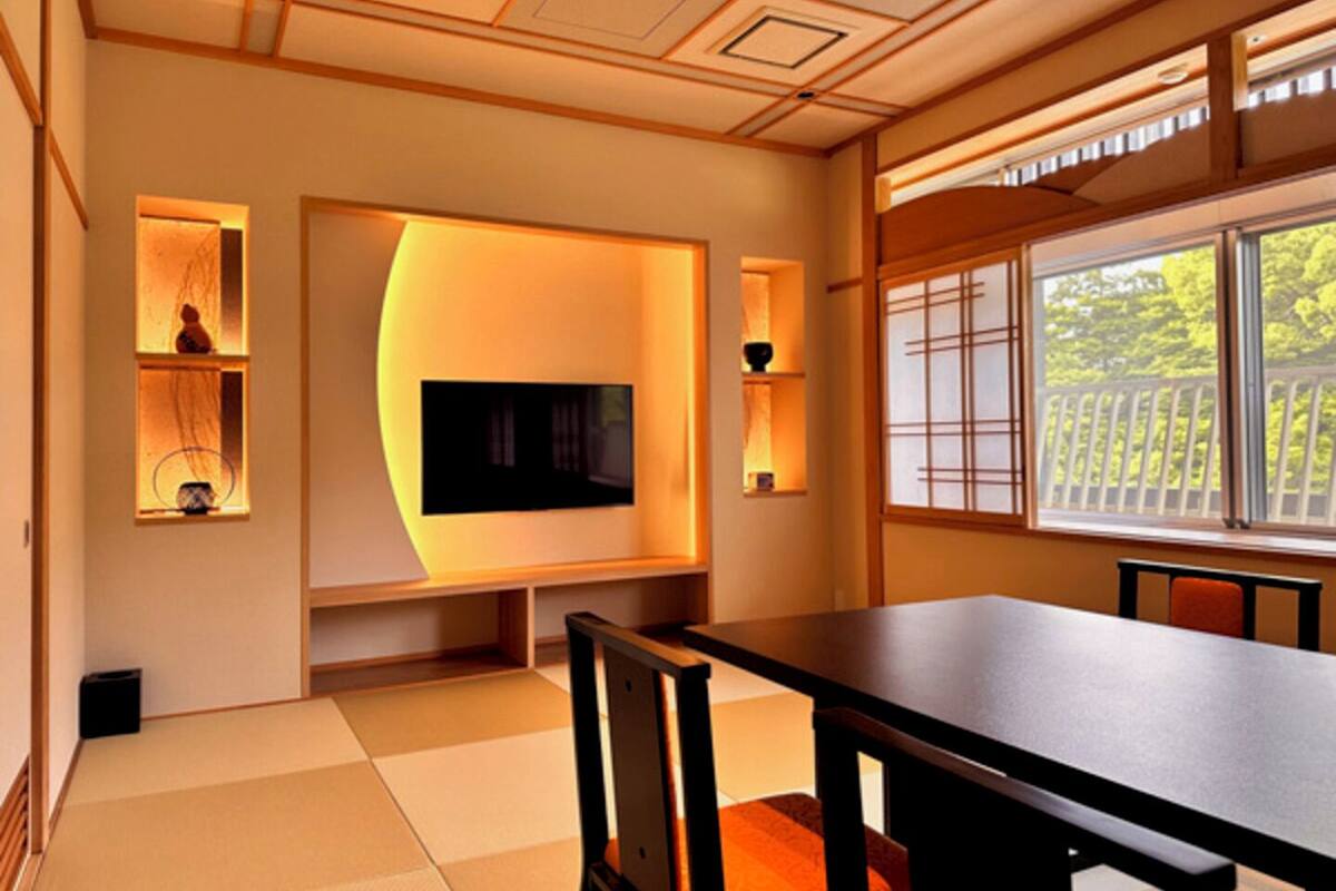 A traditional Japanese-style room with tatami flooring, a low table, and a television mounted on the wall.