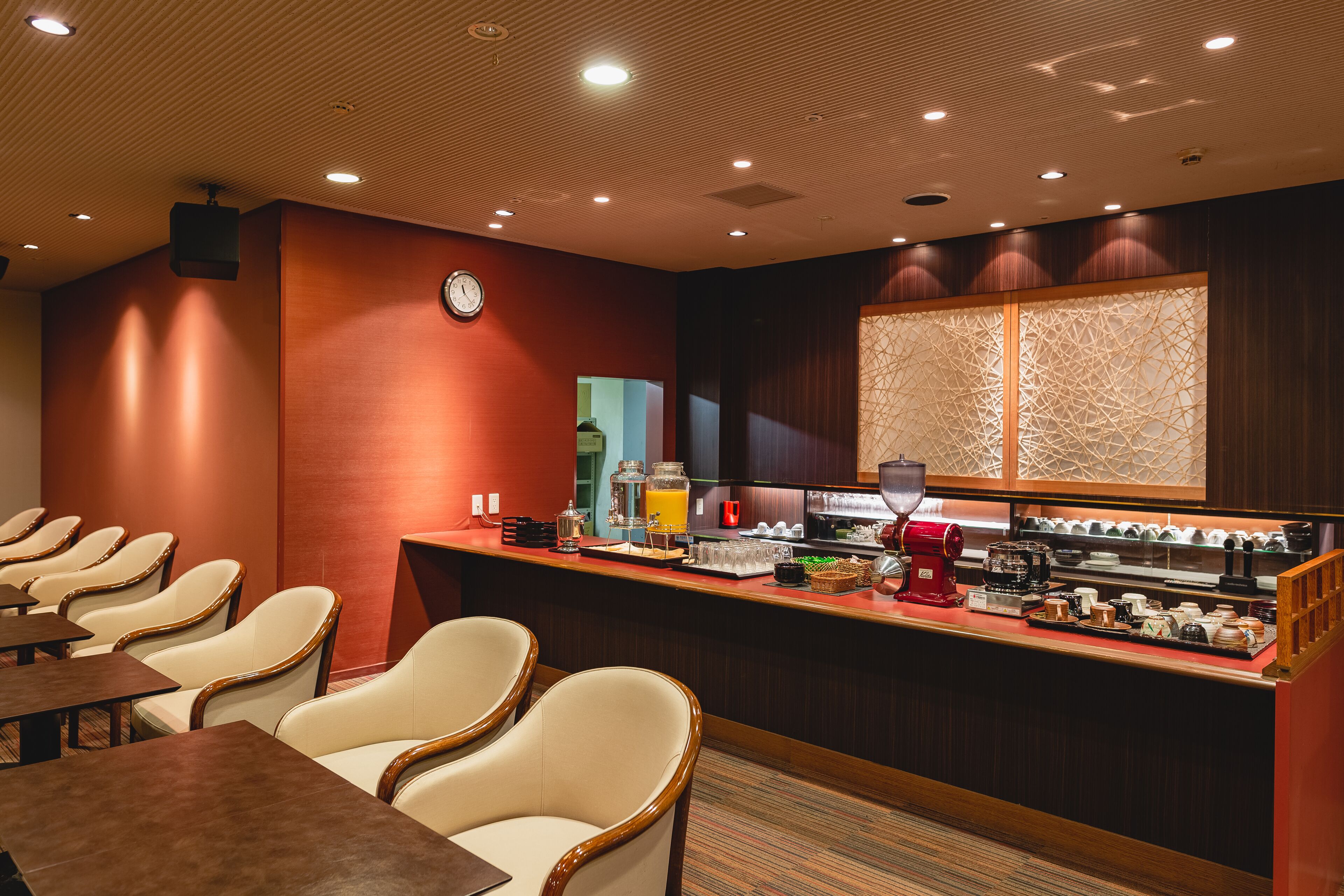 A hotel room with a breakfast bar, seating area, and a clock on the wall.