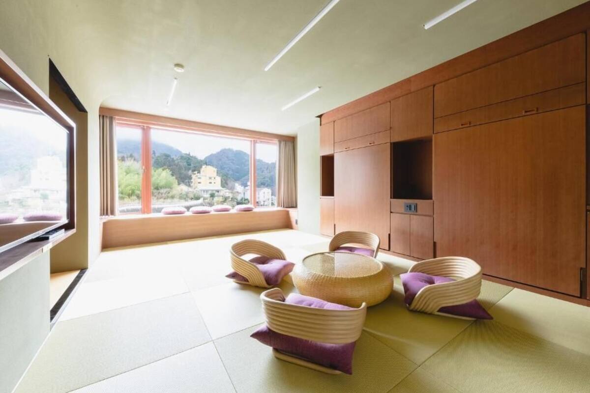 A modern room with tatami flooring, a large window with a view of mountains, and a wooden cabinet.
