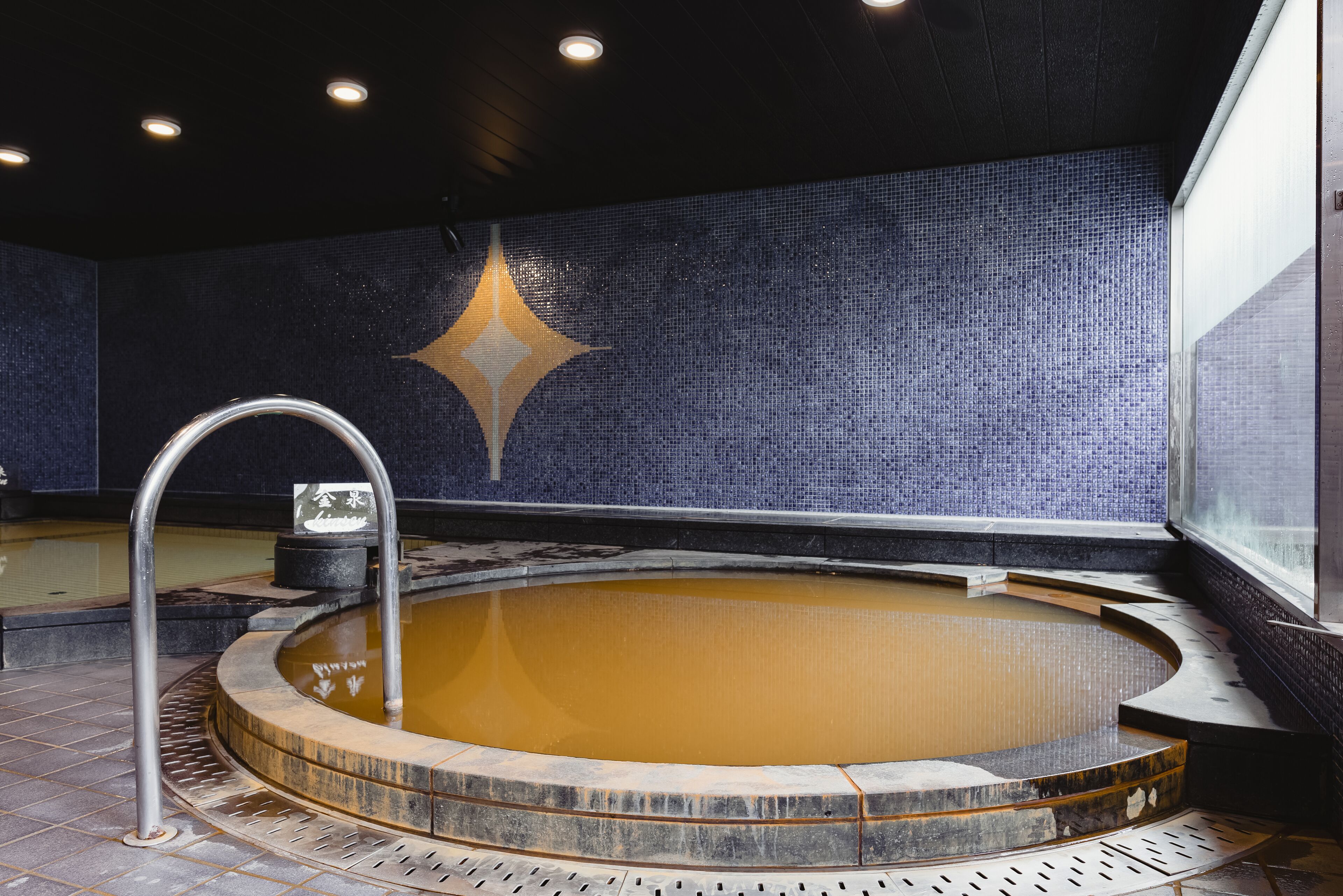 A hot tub with a tiled wall and a metal railing.