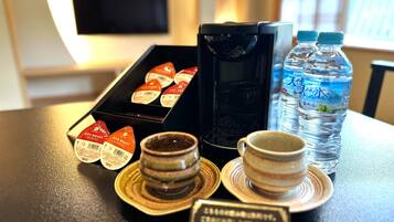 A table with a coffee maker, a box of coffee pods, two water bottles, a cup, and a small sign.
