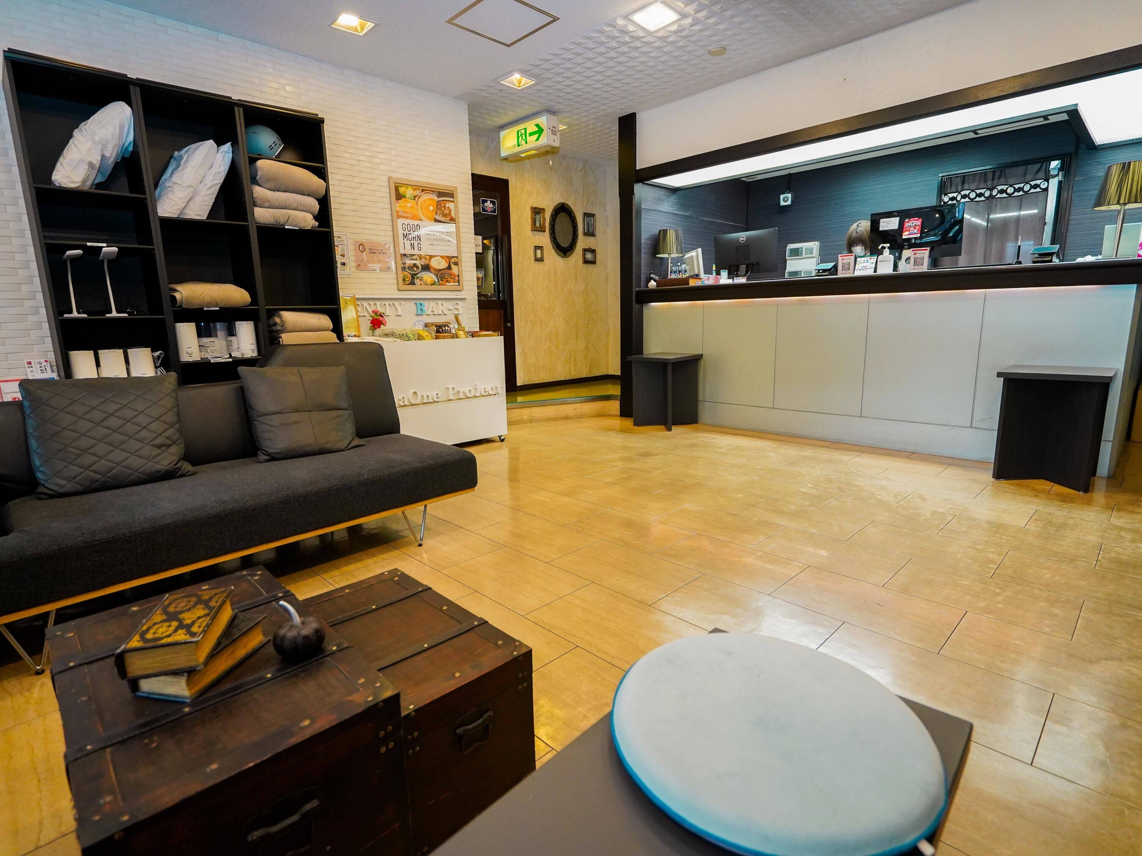 A modern hotel lobby with a sofa, a wooden coffee table, a reception desk, and a bulletin board.