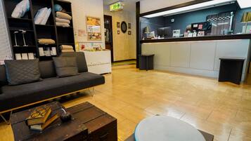 A modern hotel lobby with a sofa, a wooden coffee table, a reception desk, and a bulletin board.