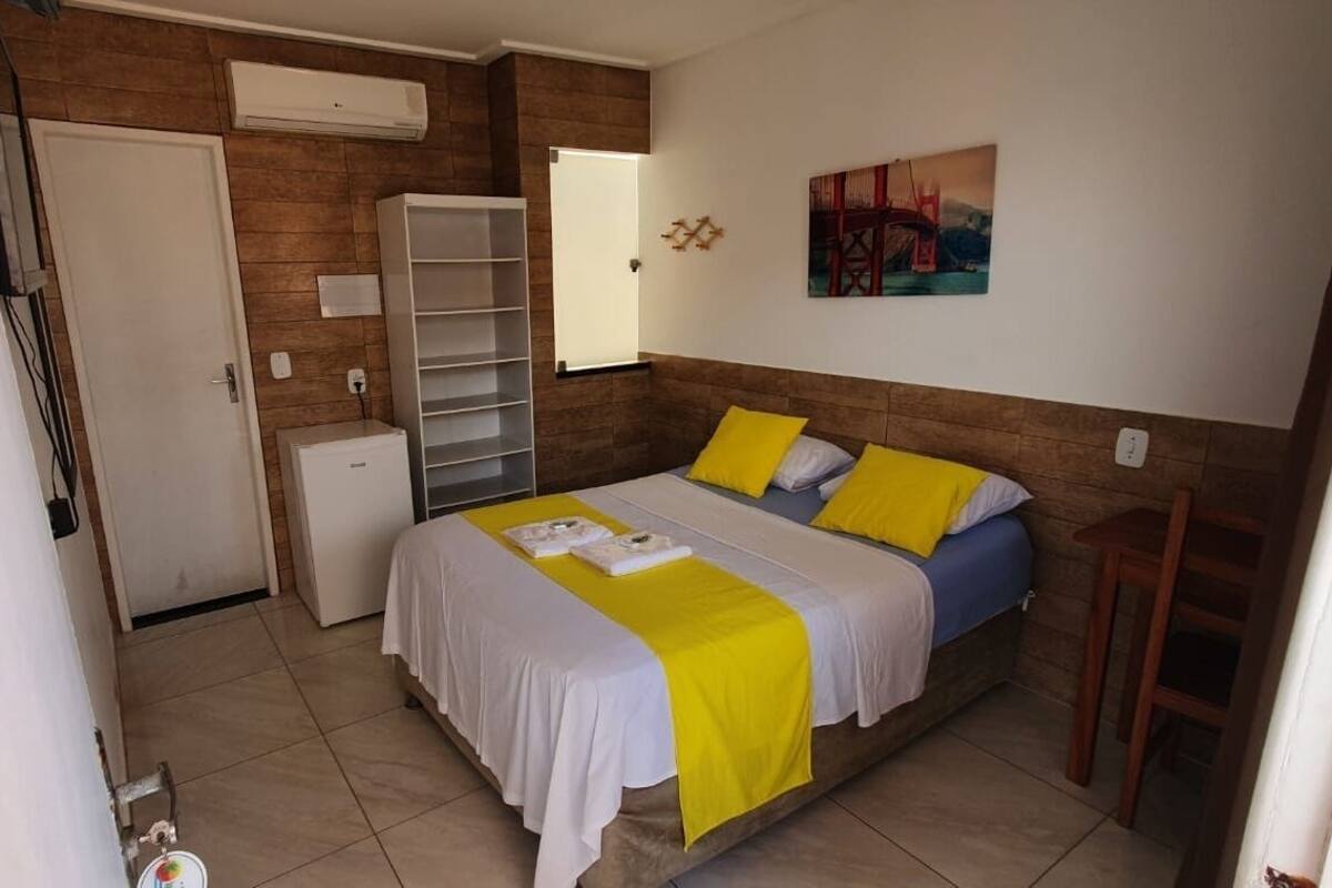 A bedroom with a bed, a white wardrobe, a small desk, and a painting on the wall.