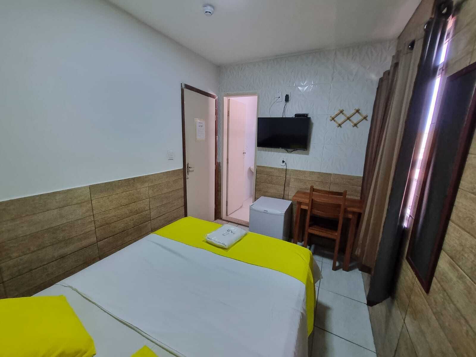 Una habitación de hotel con una cama, un escritorio pequeño, una silla, un televisor y una puerta.