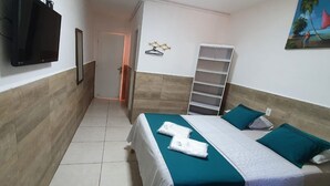 Habitació d'hotel amb un llit, una televisió, una porta, una estant i un quadre.