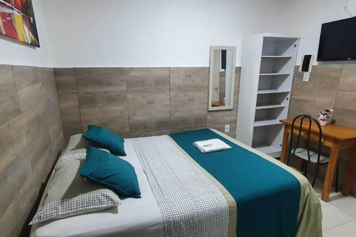 A compact room with a bed, a small desk, and a TV mounted on the wall.