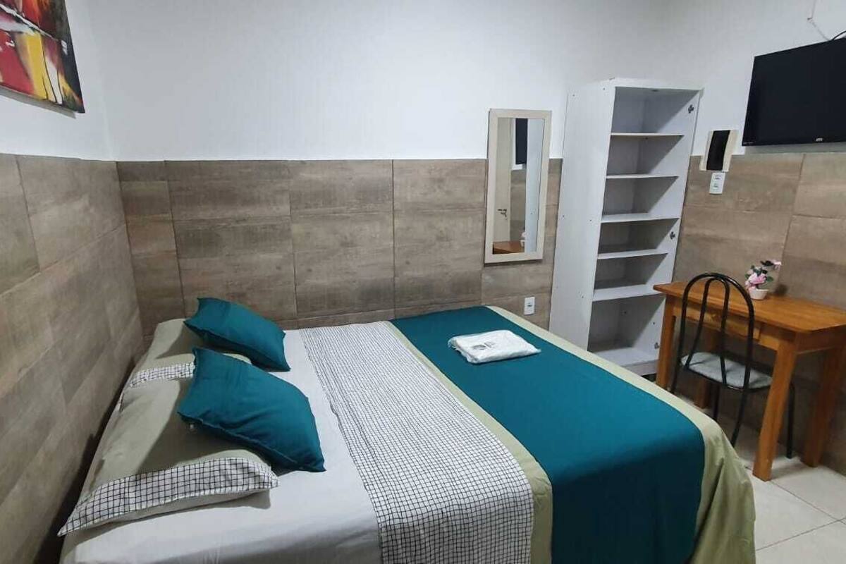 A small, compact room with a bed, a desk, a chair, a TV, and a mirror.