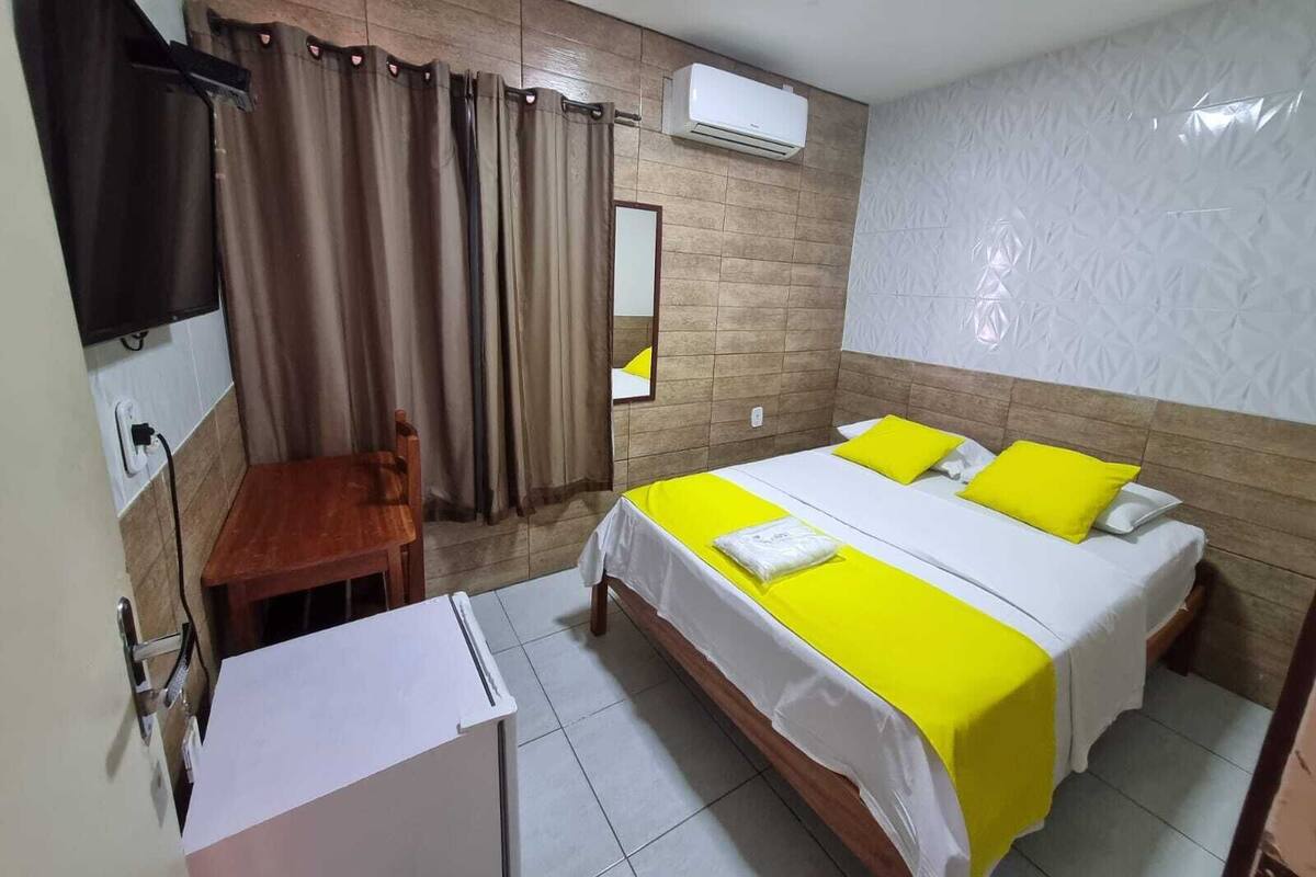 A hotel room with a bed, a desk, a chair, an air conditioner, and a television.