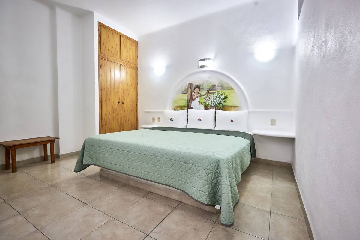 Ein Schlafzimmer mit einem Bett, einem Holzschrank, einer Bank und einem an der Wand befestigten Regal.