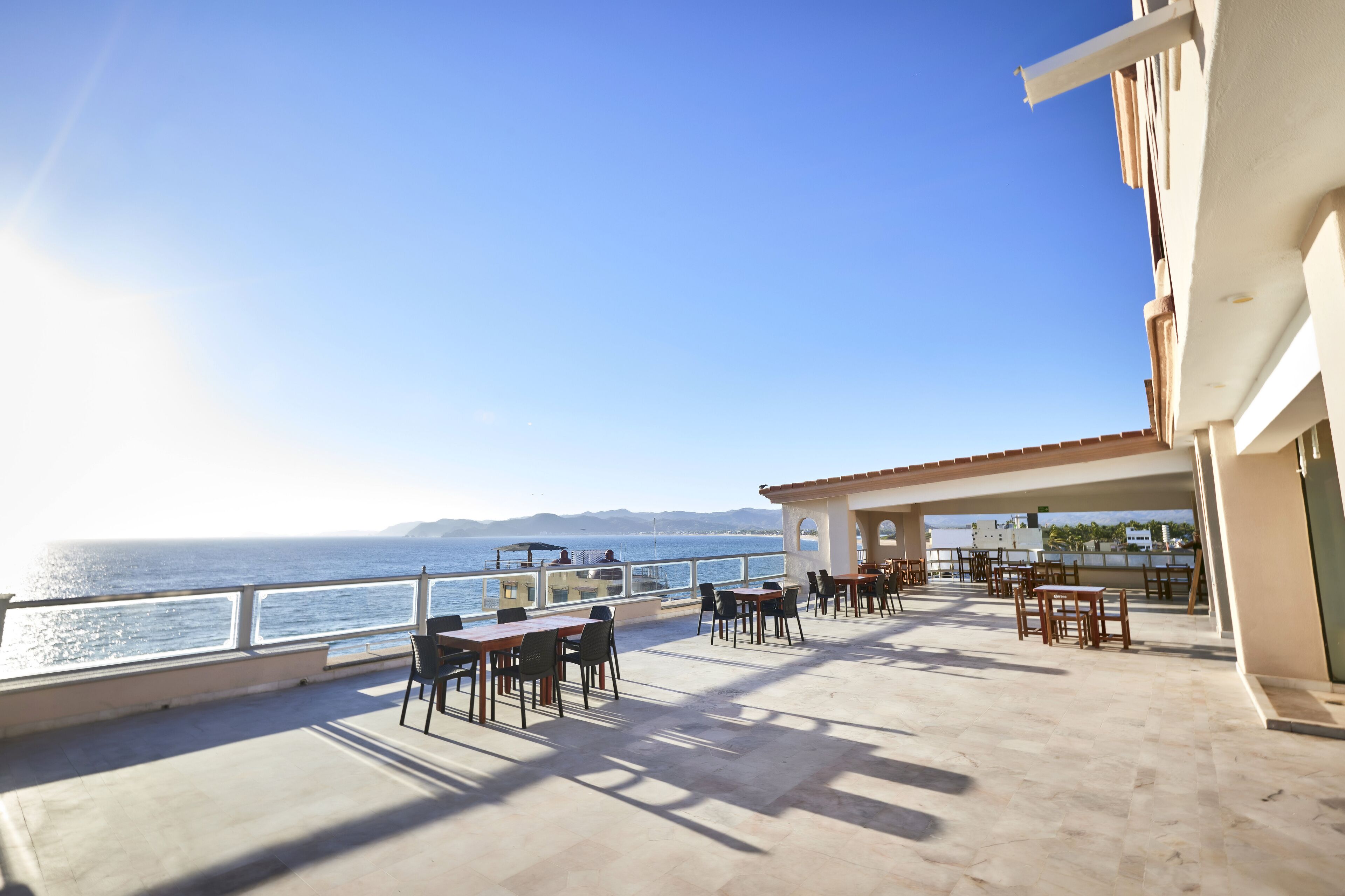 An outdoor terrace with tables and chairs, overlooking a body of water and distant mountains.