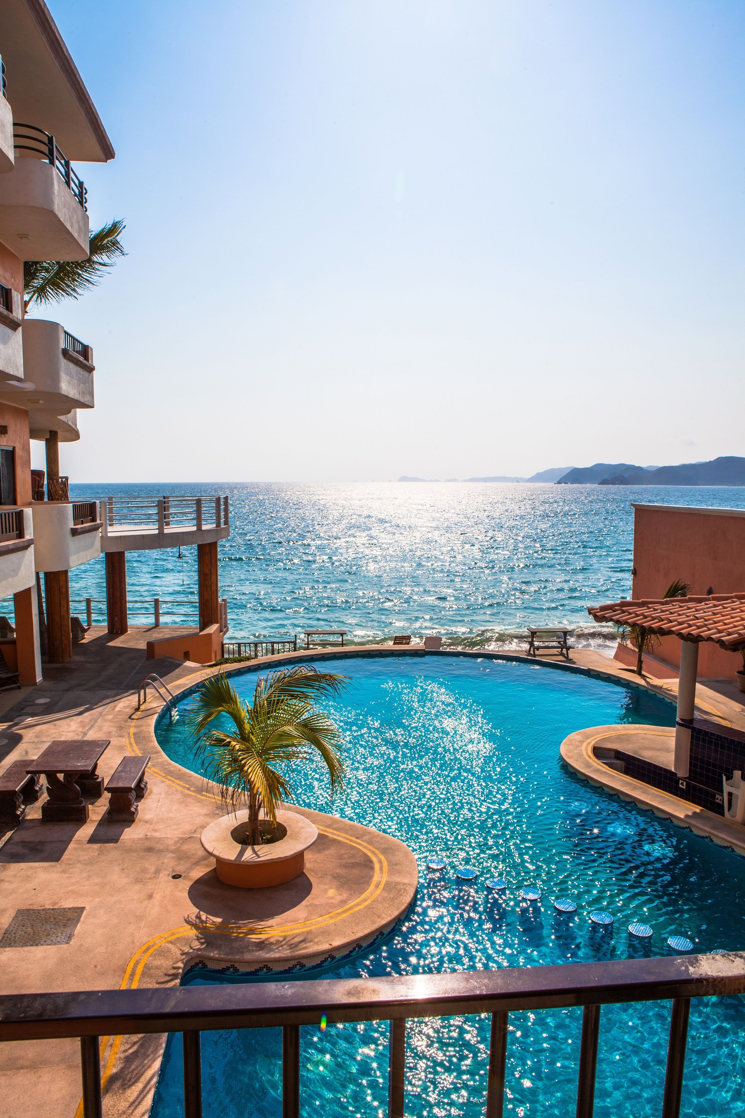 Una piscina con vista al mar, una palmera y un edificio con balcones.