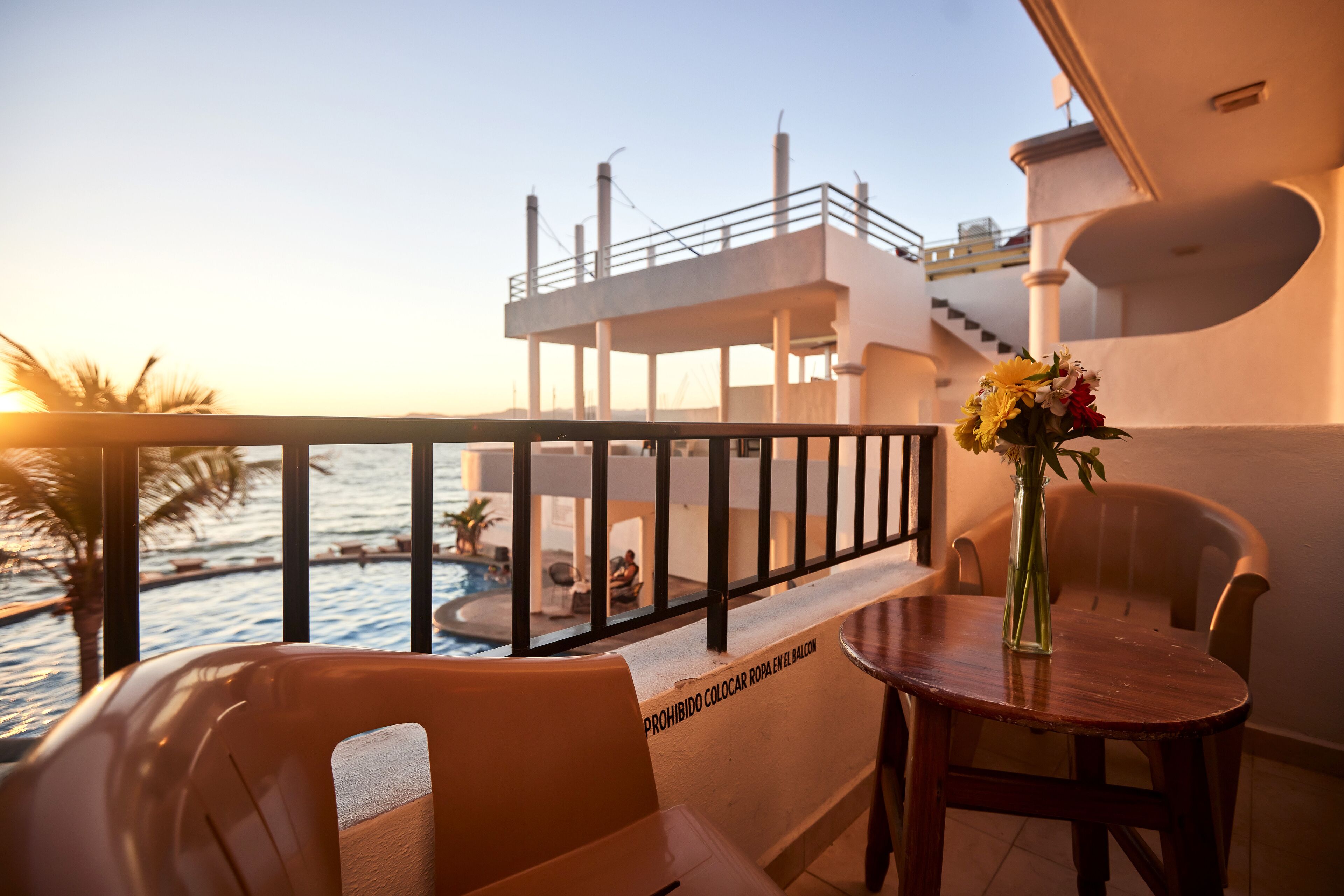A balcony with a view of the sea, a pool, and a dining area with a table and chairs.