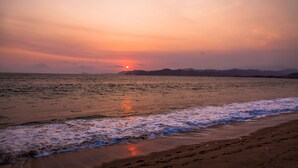 A beach with waves at sunset, distant mountains, and a clear sky.