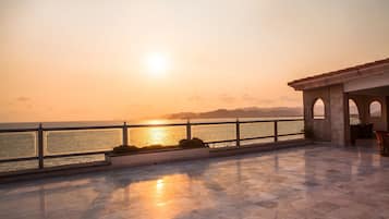 Una terraza con vistas al mar al atardecer, con suelo de baldosas y barandilla.