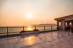 Una terraza con vistas al mar al atardecer, con suelo de baldosas y barandilla.