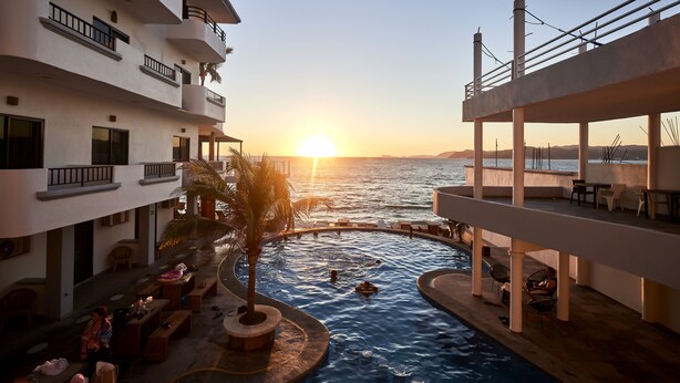 A pool area with a sunset view, outdoor seating, and a palm tree.
