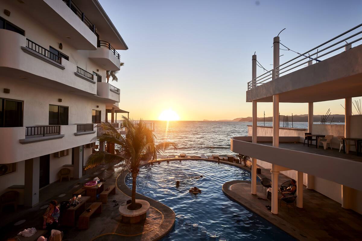 Ein Poolbereich mit Sonnenuntergangsblick, Sitzgelegenheiten im Freien und einer Palme.
