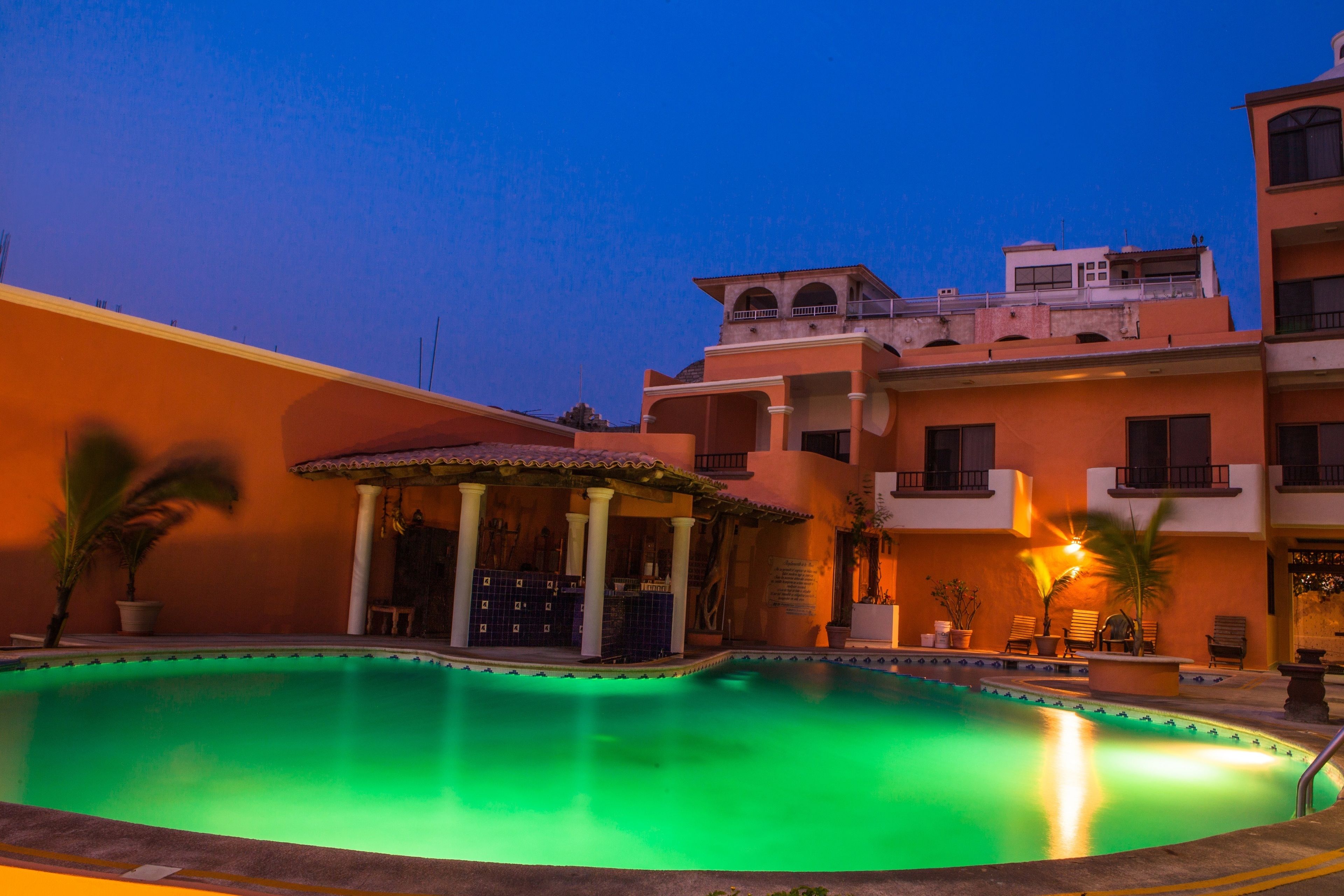 A swimming pool with a covered area, surrounded by buildings with balconies and a clear sky.
