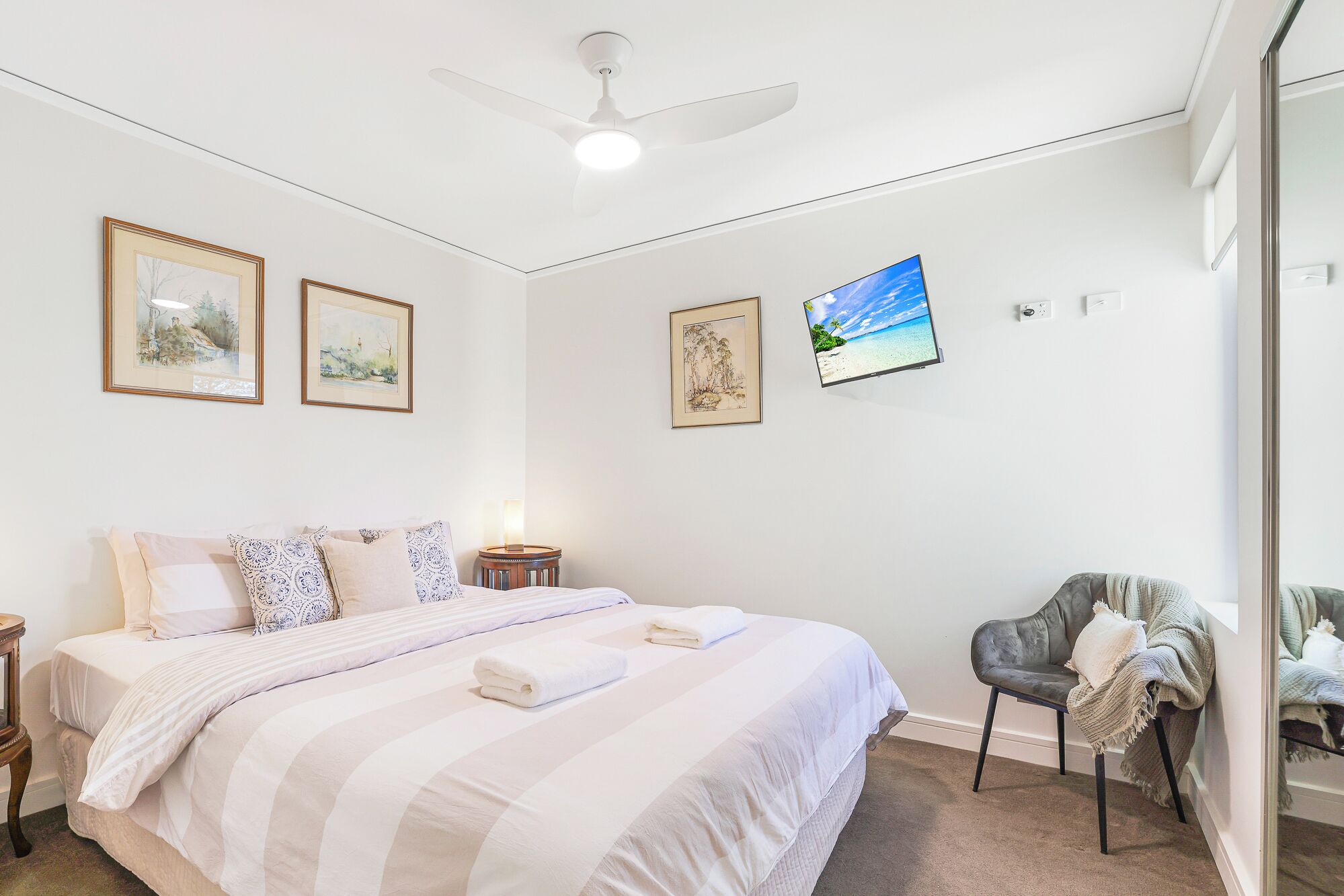A bedroom with a bed, a chair, and a TV. There are framed pictures on the wall.