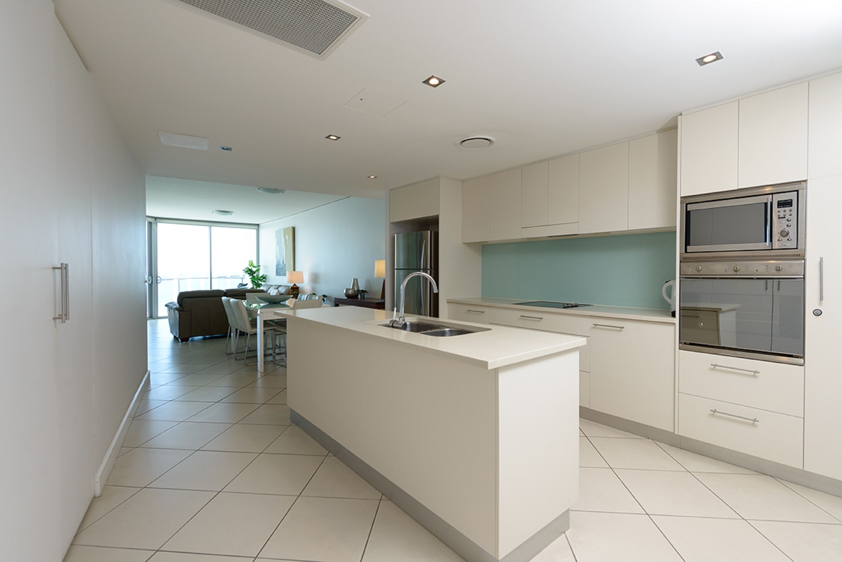Una cocina moderna con armarios blancos, una isla central con pileta y electrodomésticos integrados, incluyendo un microondas y horno.