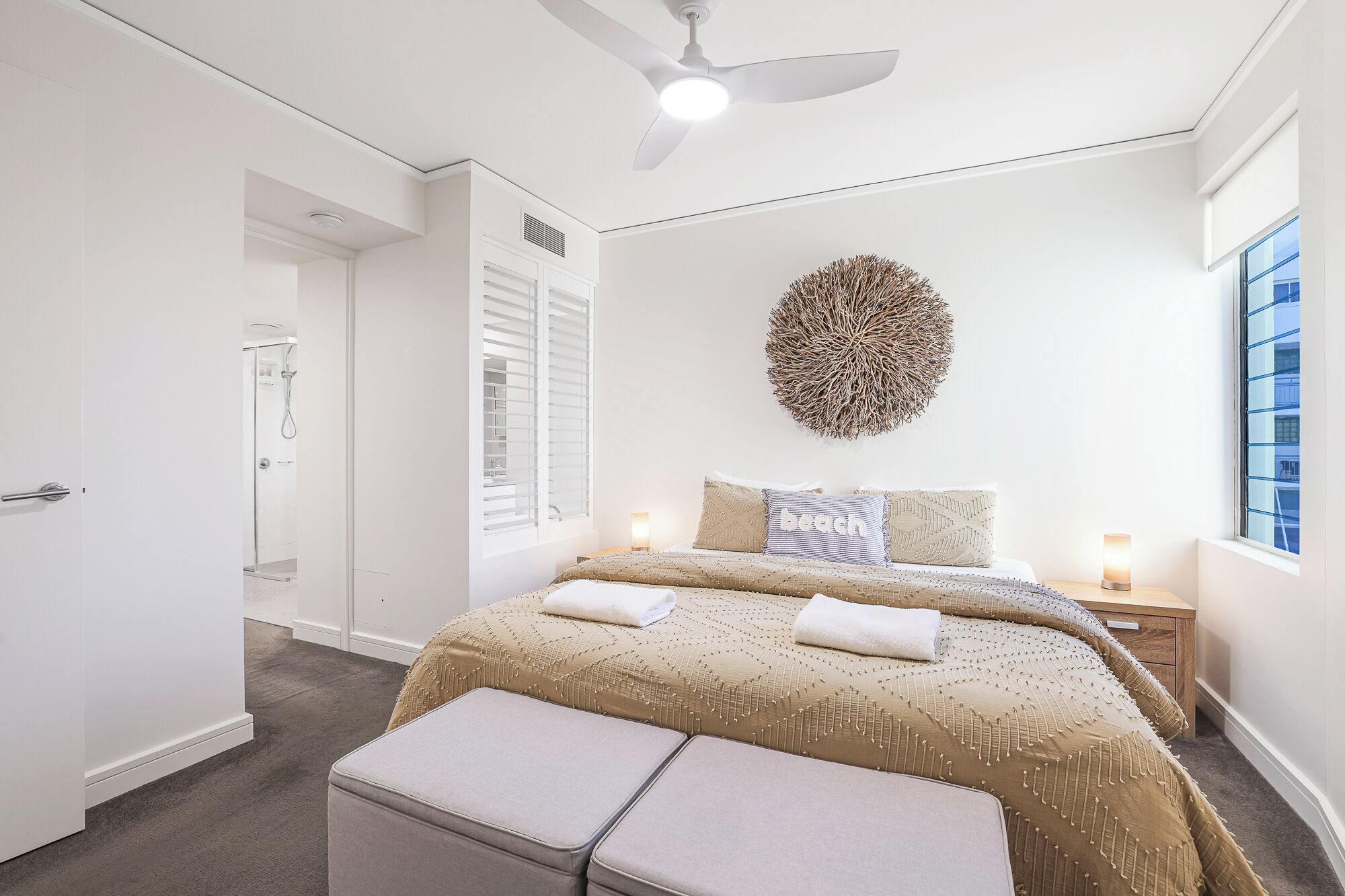 Un dormitorio con cama, ventilador de techo, un adorno en la pared y ventana con persianas.