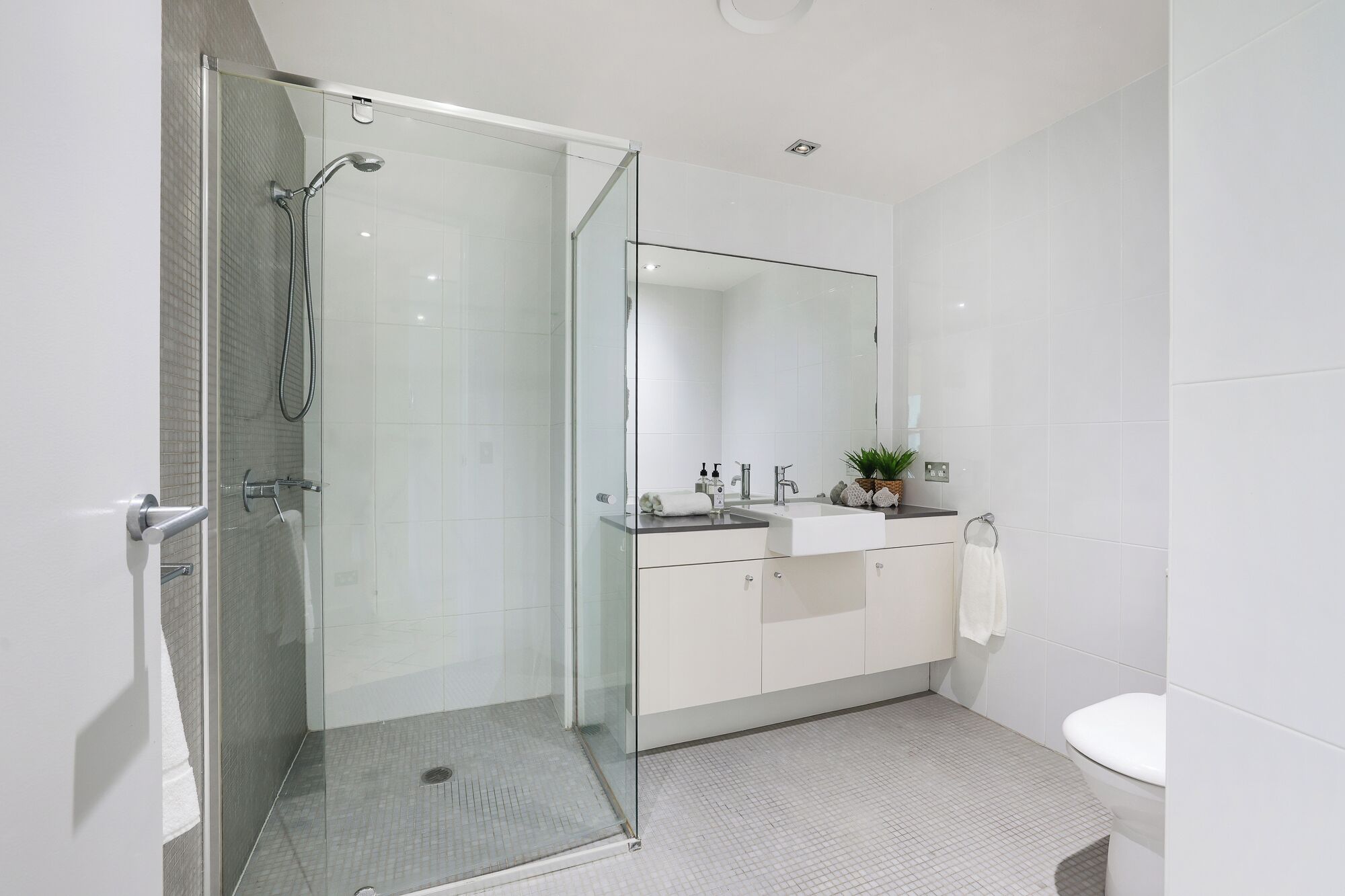 Un baño moderno con cabina de ducha de vidrio, lavabo con espejo y un inodoro.