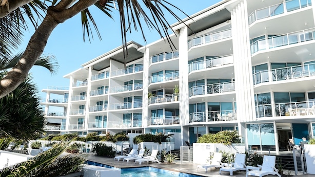 A modern hotel with multiple balconies, a swimming pool, and lounge chairs.