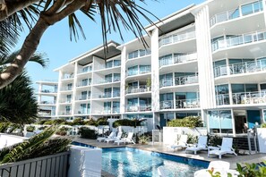 A modern hotel with multiple balconies, a swimming pool, and lounge chairs. - C Bargara Resort (Bargara)