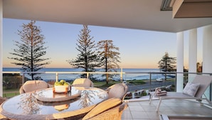 A balcony with wicker furniture, a glass table, and a view of the ocean and trees.