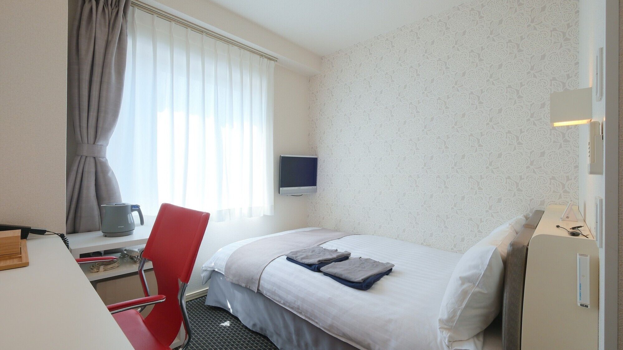 Ein Hotelzimmer mit einem Bett, einem Schreibtisch mit Stuhl, einem Fernseher und einem Wasserkocher.