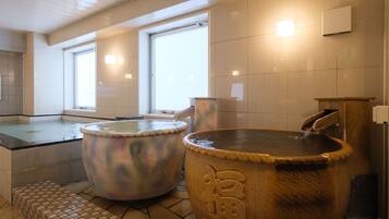 A traditional Japanese onsen with two large hot tubs, a tiled floor, and a window providing natural light.