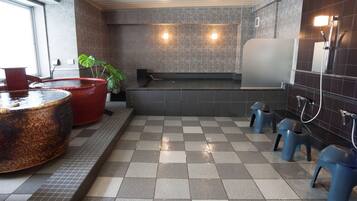 Eine öffentliche Toilette mit Schachbrettboden, roten und blauen Hockern, einem großen Waschbecken und einem wandmontierten Spiegel.