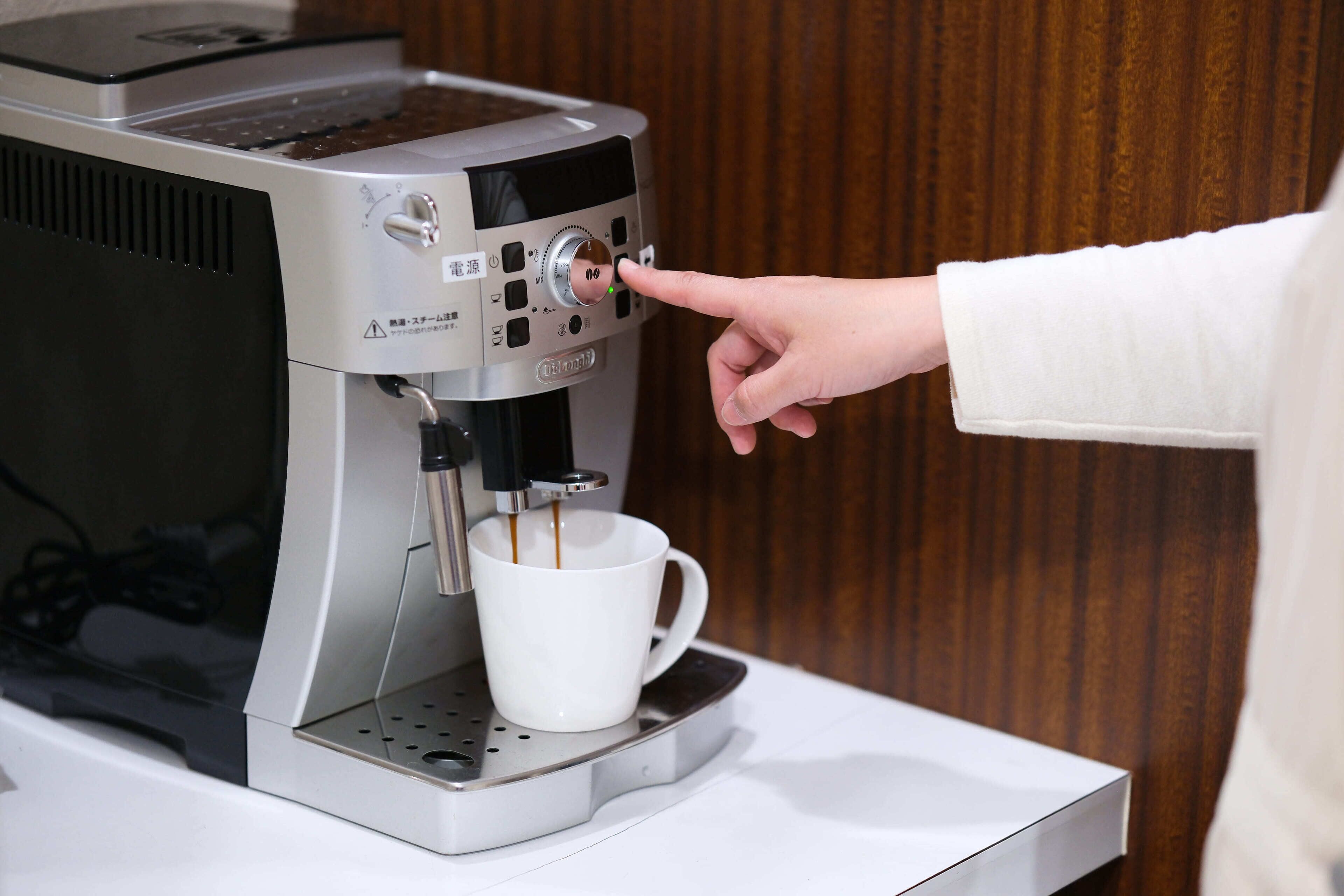 Eine Hand justiert eine Kaffeemaschine, darunter ein Kaffeebecher.