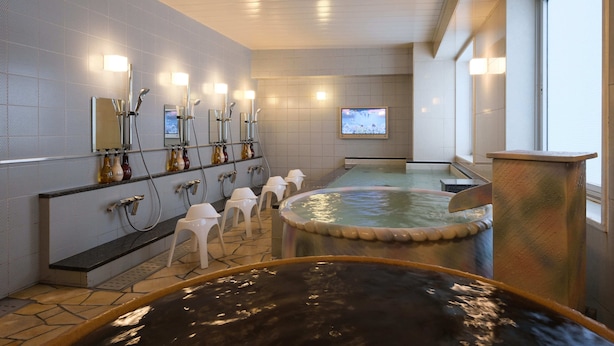 Un moderno espacio de spa con varias jacuzzis, una pantalla de televisión y una fila de lavamanos con espejos.