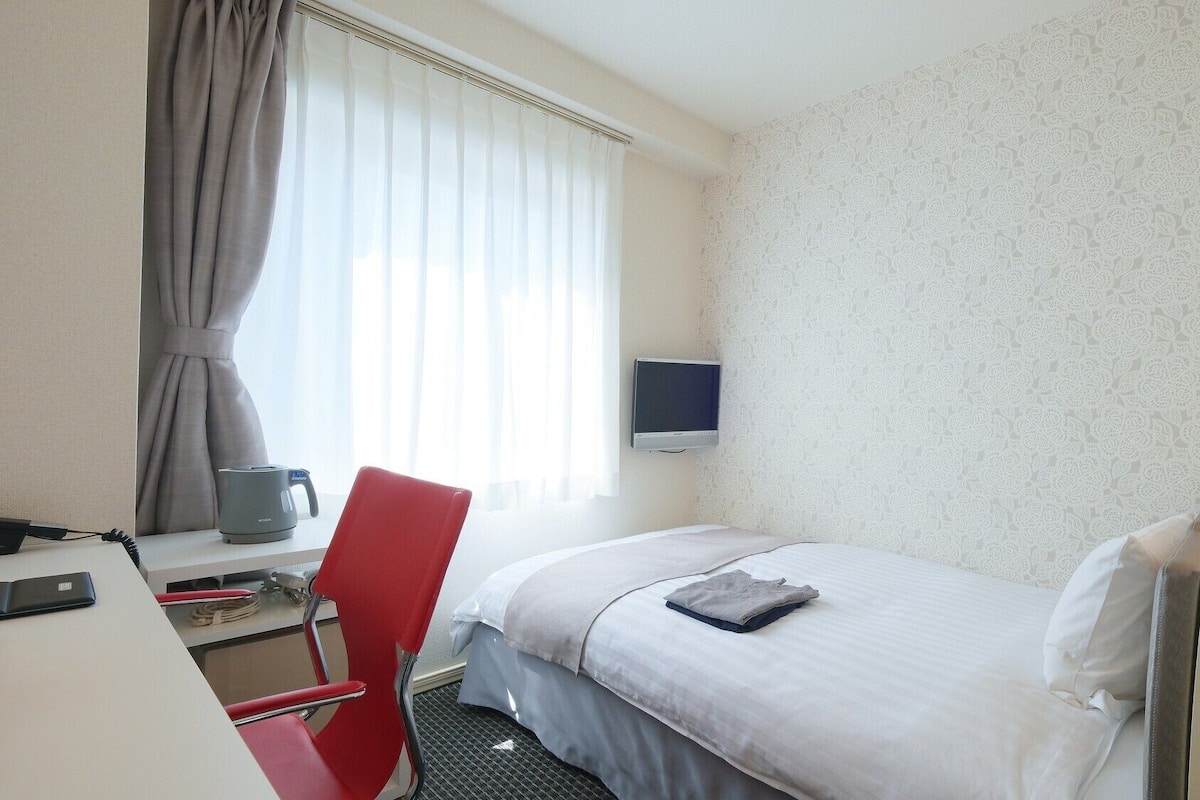 Une chambre d’hôtel comprenant un lit, un bureau avec un ordinateur, une chaise, une télévision et une fenêtre avec des rideaux.