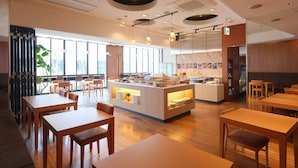 Un restaurante moderno con mesas y sillas de madera, una barra central con exhibición y grandes ventanales que permiten la entrada de luz natural.