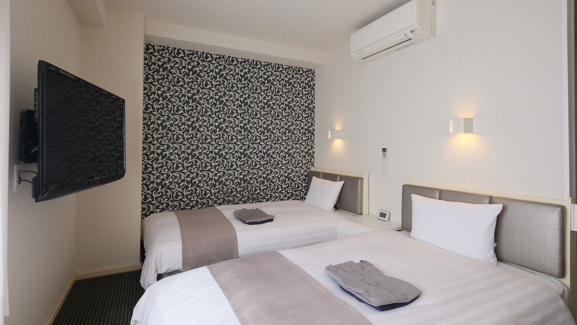 Ein Hotelzimmer mit zwei Betten, einem Flachbildfernseher, einer Klimaanlage und einer Wandtapete mit Muster.