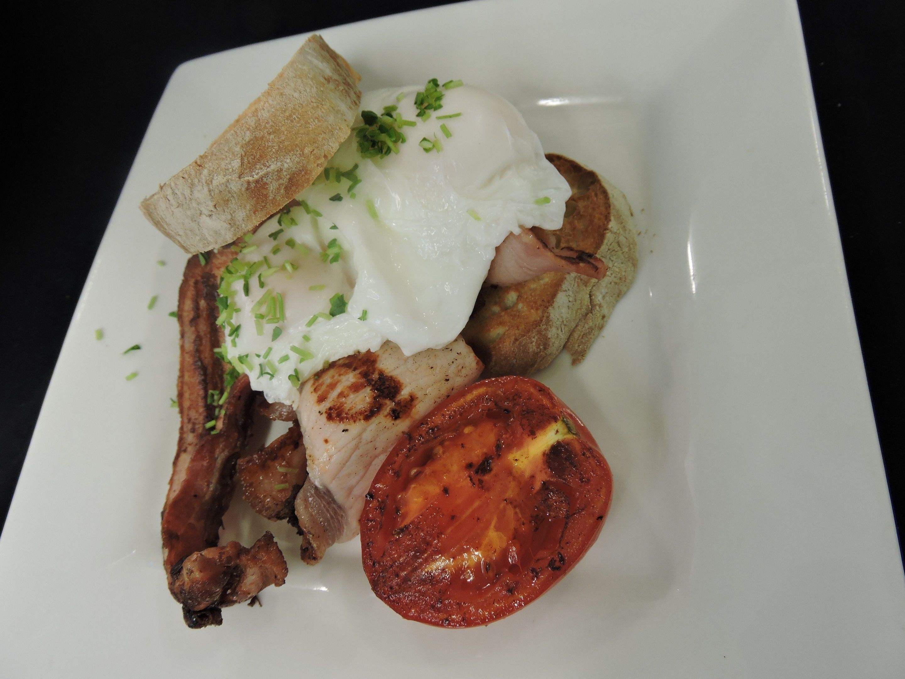 Une assiette avec un œuf poché, du bacon, une tomate grillée et des toasts.